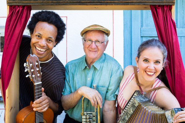 Hans Well, Sarah Well und Komale schauen mit Instrumeneten (Gitarre, Trompete, Ziehharmonika) aus einem alten Kaspertheater heraus
