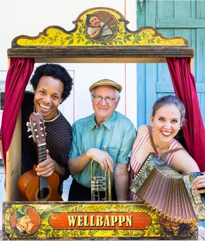 Hans Well, Sarah Well und Komale schauen mit Instrumeneten (Gitarre, Trompete, Ziehharmonika) aus einem alten Kaspertheater heraus