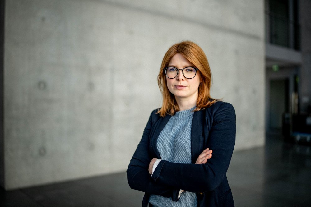 Marlene Schönberger steht - ernst schauend - mit verschränkten Händen vor einer Betonwand. Sie trägt unter einer dunkelblauen Jacke einen hellblauen Strickpulli