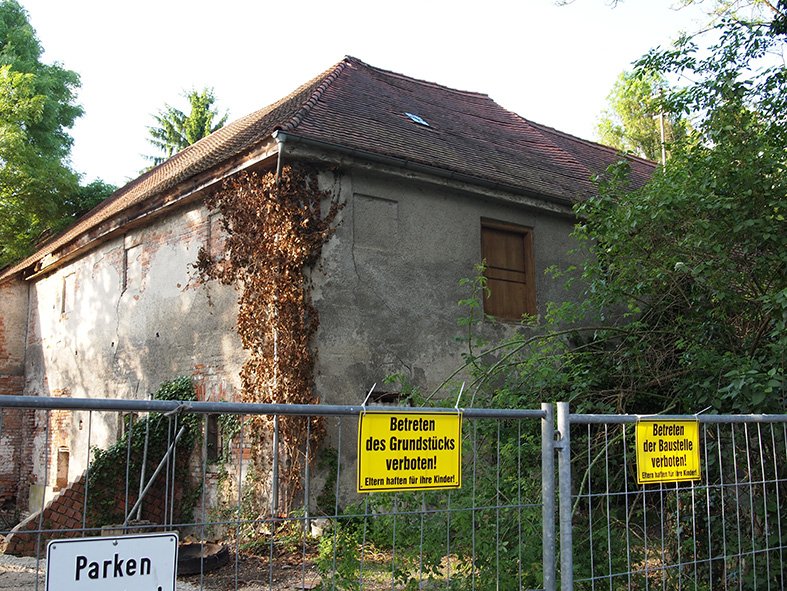 Bauzaun mit "Betreten verboten"-Schildern; dahinter ungepflegtes Haus