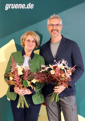 Spitzenduo Iris Haas und Christoph Rabl mit bunten Blumensträußen vor einem Grünen-Rollup