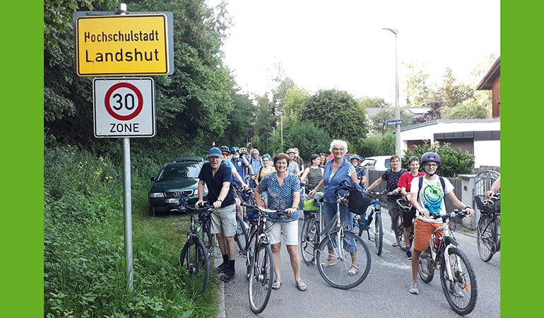 viele Radfahrer warten auf der Roßbachstraße vor dem Ortsschild "Hochschulstadt Landshut"