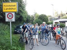 viele Radfahrer warten auf der Roßbachstraße vor dem Ortsschild "Hochschulstadt Landshut"
