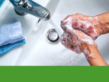 unter einem laufenden Wasserhahn waschen sich zwei eingeschäumte Hände, ein Stück Seife liegt am Waschbeckenrand