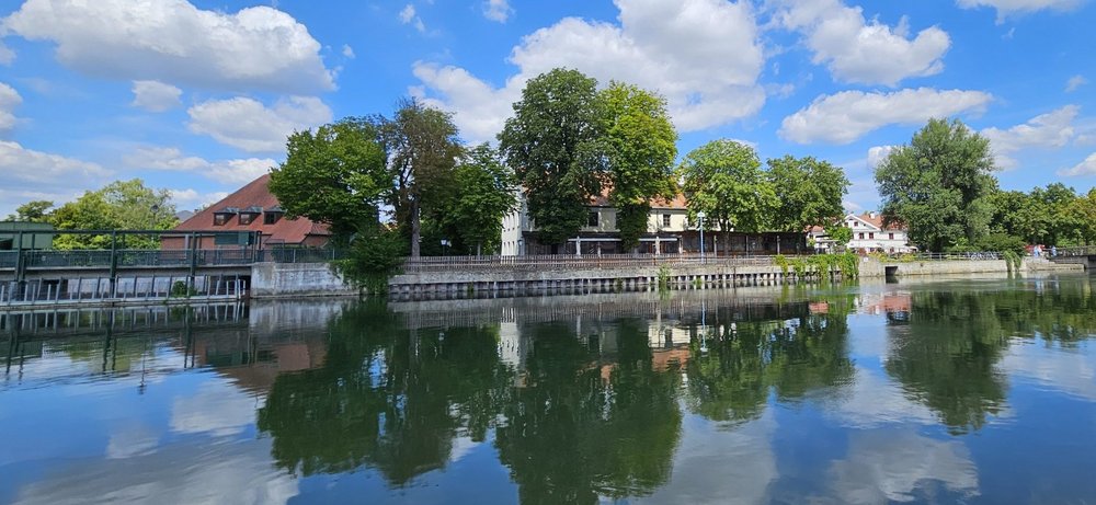 das Gasthaus "Zur Insel" mit Biergarten unter Bäumen von der Altstadtseite aus betrachtet, im Vordergrund die Isar