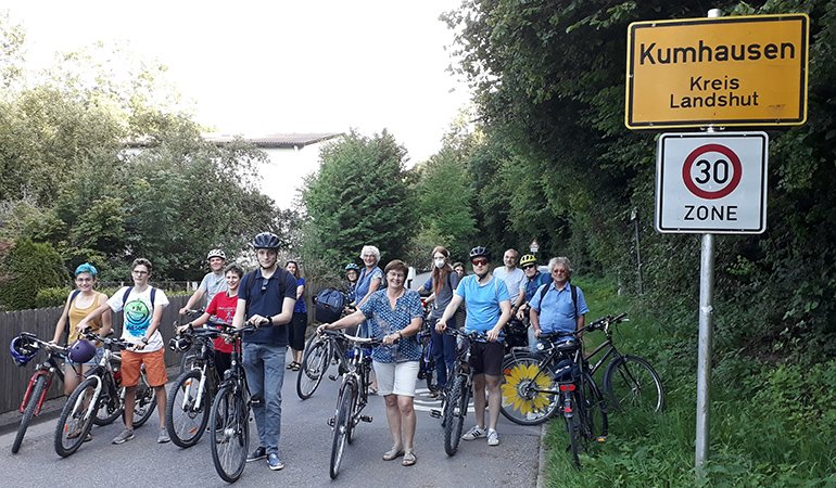 viele Radfahrer warten auf der Roßbachstraße vor dem Ortsschild "Kumhausen"