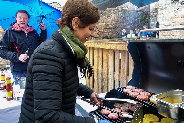 Stefan Gruber hält einen Schirm und Sigi Hagl grillt Burger im Regen