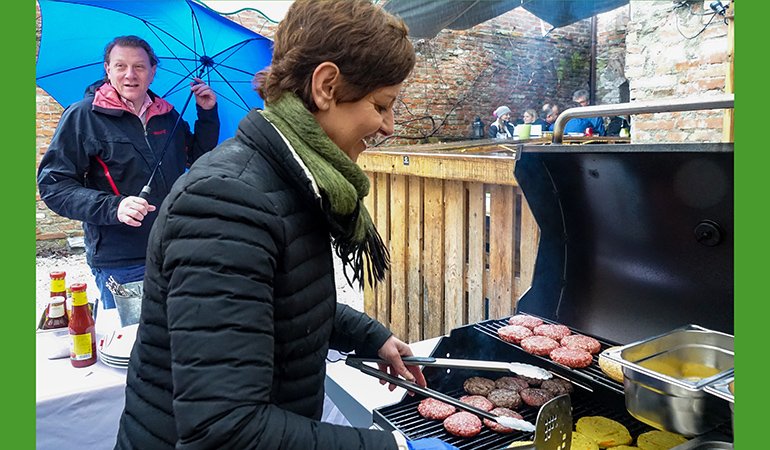 Stefan Gruber hält einen Schirm und Sigi Hagl grillt Burger im Regen