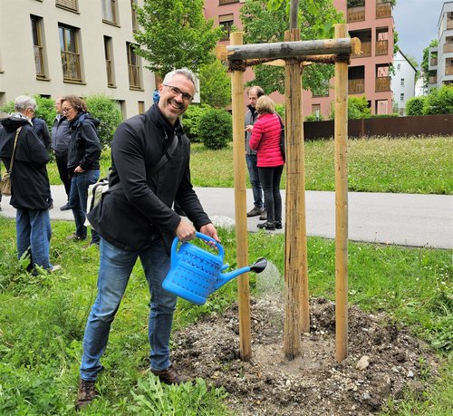 Christoph Rabl gießt einen frisch gepflanzten Baum; im Hintergrund einige Baumpat*innen