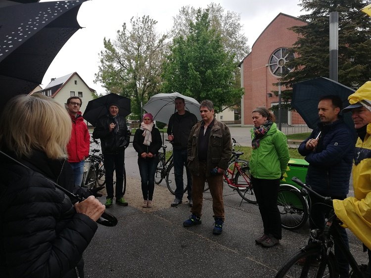 Menschen unter Regenschirmen stehen im Kreis am Wolfgangsplatz und diskutieren