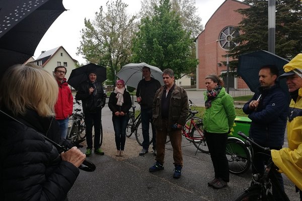 Menschen unter Regenschirmen stehen im Kreis am Wolfgangsplatz und diskutieren