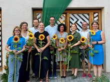 MdB Marlene Schönberger, Laura Pollard, Ferdinand Schoßer, Julia Oberland, Marek Cina, Dr. Simone Hartmann, MdL Mia Goller, Rudi Ruhland, Prof. Dr. Hannah Jörg mit Sonnenblumen in der Hand vor grüner Beach-Flag