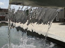Foto eines von oben fließenden, breiten Wasserrstrahls aus einem Brunnen - von hinten fotografiert durch das Wasser hindurch