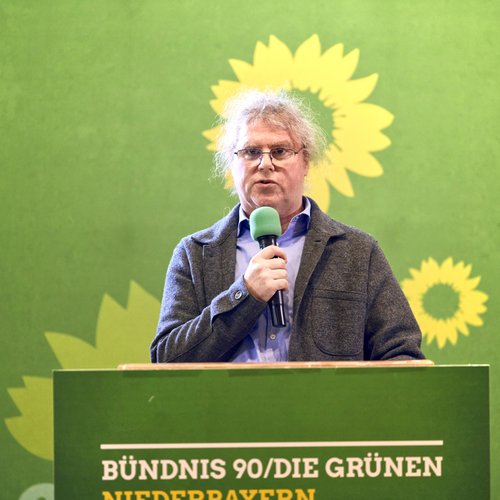 Bezirksrat Markus Scheuermann spricht in Mikrofon vor grünem Hintergrund, Platz 2 Bezirkstagsliste