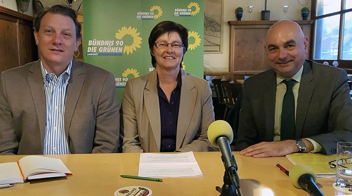 OB-Kandidat Stefan Gruber, Rosi Steinberger und Jürgen Mistol, beide MdL im Wintergarten des Gasthauses Insel vor einem Grünen-Aufsteller am Tisch sitzend