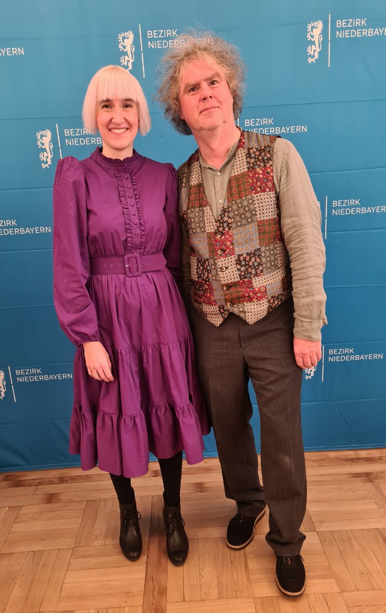 Stefanie Auer und Markus Scheuermann vor einer blauen Stellwand mit vielen Aufschriften "Bezirk Niederbayern"