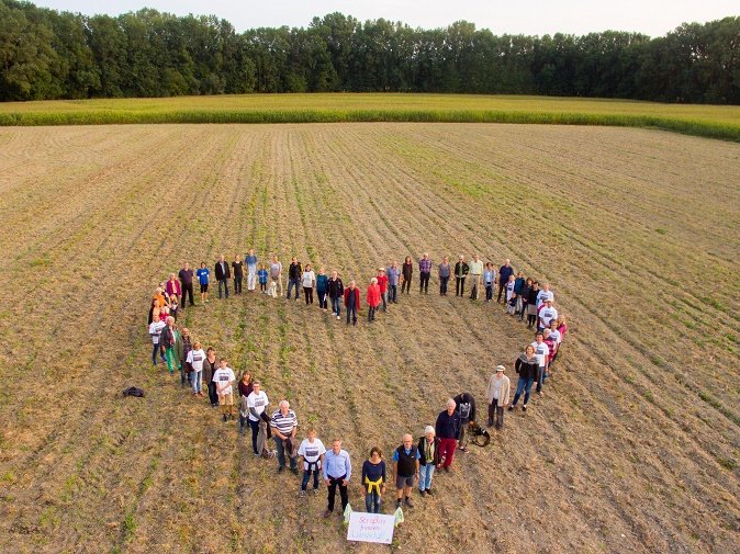 Viele Menschen stehen in Herzform auf einem abgeernteten Feld nahe der geplanten Trasse der Westtangente.